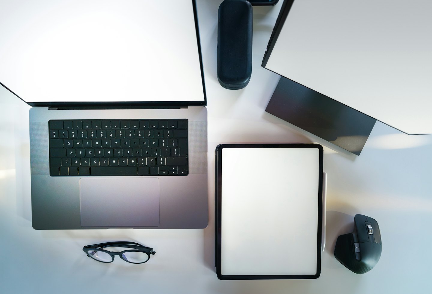 Moderno spazio di lavoro digitale con laptop, tablet e monitor su una scrivania bianca.